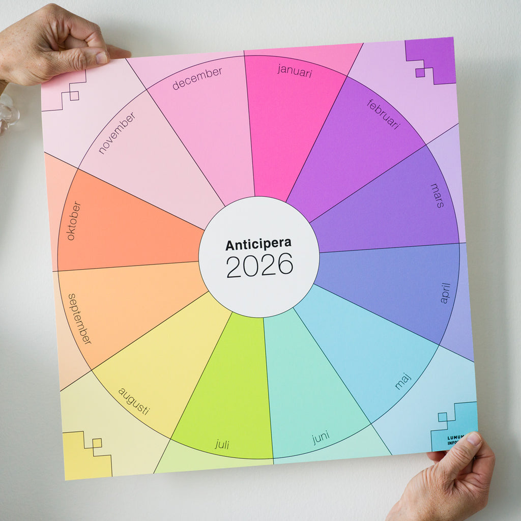 Två händer håller Anticipera Väggplanerare i stilen Emelie, i färgerna gammelrosa, fräsch rosa, lila med indigo, och gult med grönt och orange, mot en vit vägg. 