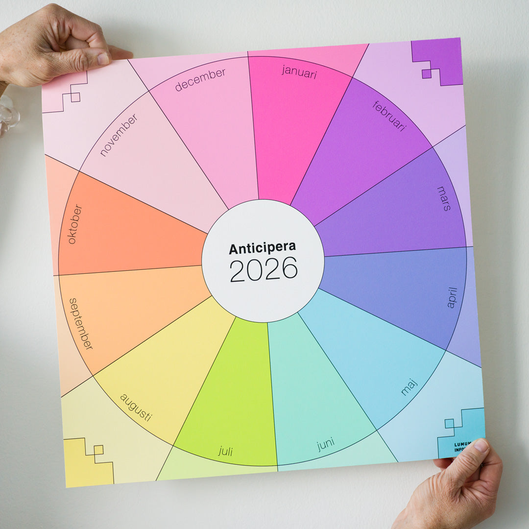 Två händer håller Anticipera Väggplanerare i stilen Emelie, i färgerna gammelrosa, fräsch rosa, lila med indigo, och gult med grönt och orange, mot en vit vägg. 